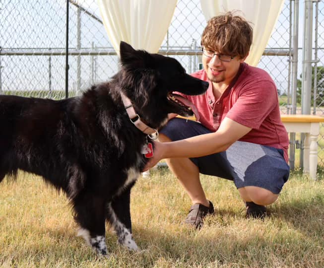 young man gently pet a black dog